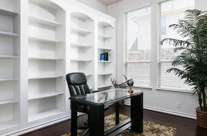 Office with empty shelves and black desk with glass top