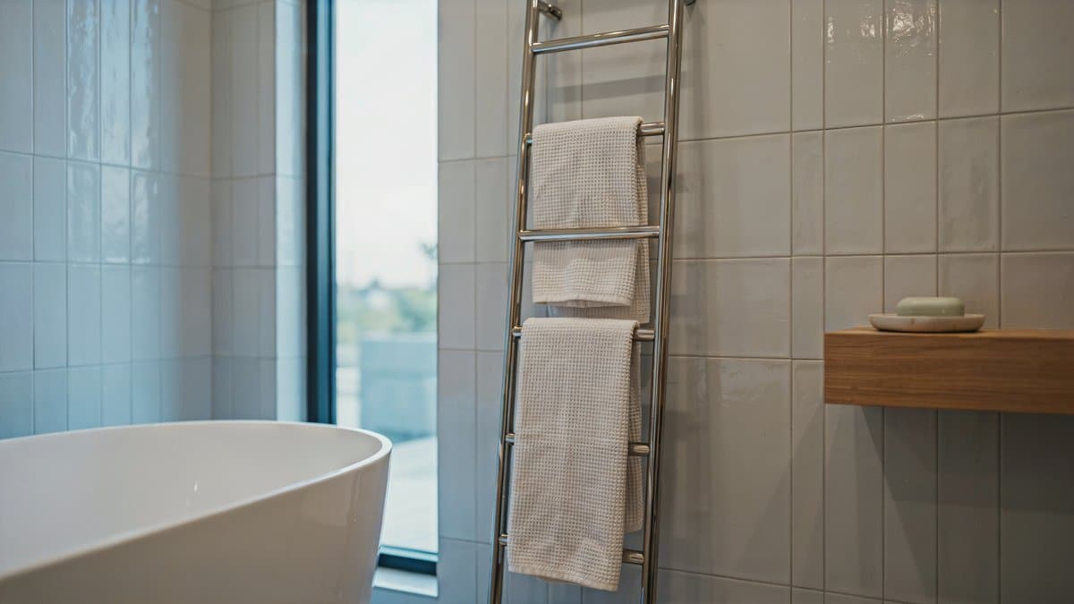 Ladder style rack with chrome rungs holding cream waffle weave towels by a tub
