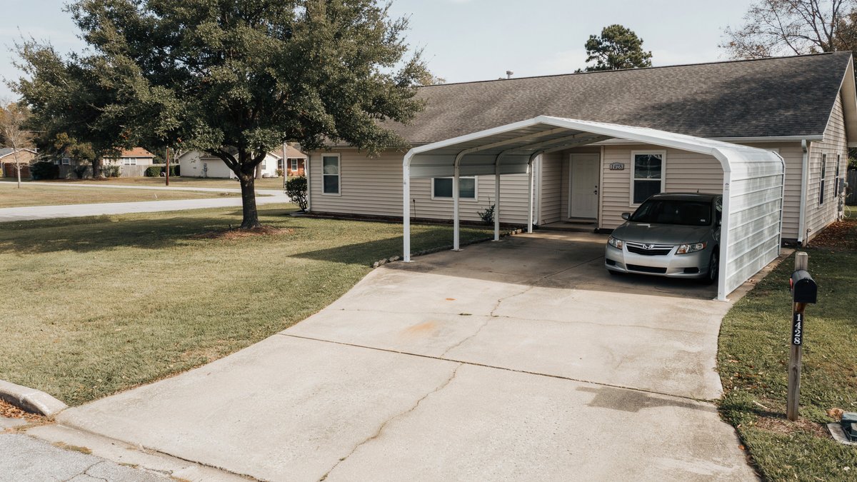 Metal carport attached to a beige suburban house with a silver sedan underneath
