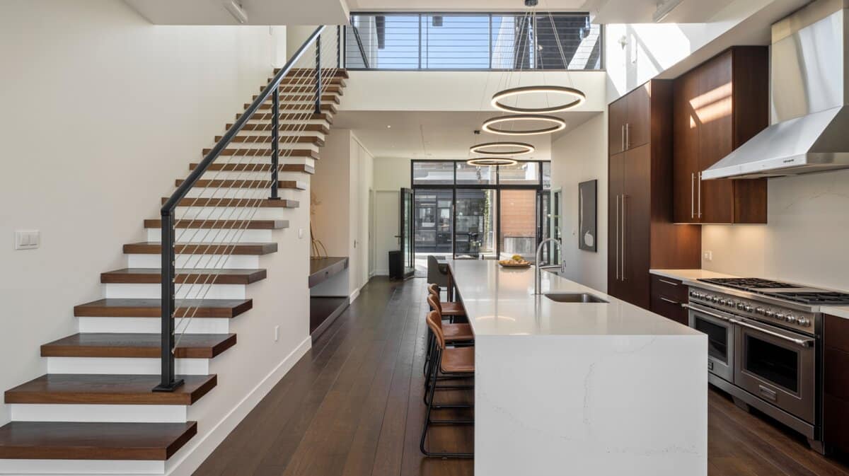 Modern open concept home with floating dark steps and cable railing next to white galley kitchen with professional range