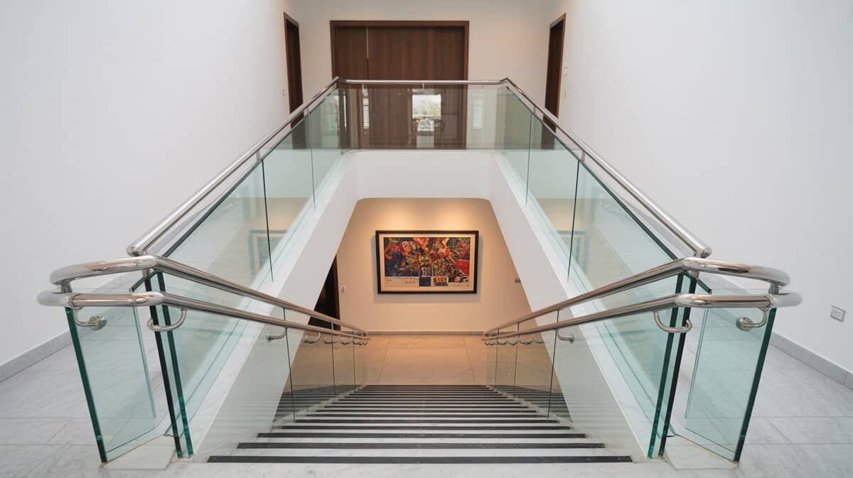 Modern staircase with frameless glass panel balusters and chrome handrail on white marble steps looking up