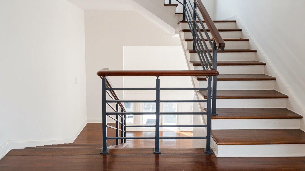 Modern staircase landing with black horizontal bar railing on dark wood treads and white risers