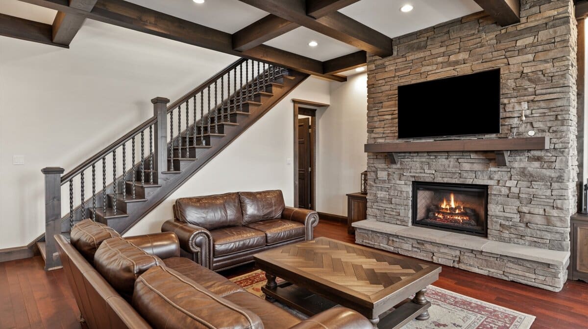Rustic mountain home living room with staircase featuring dark metal balusters and dark wood handrail by stone fireplace