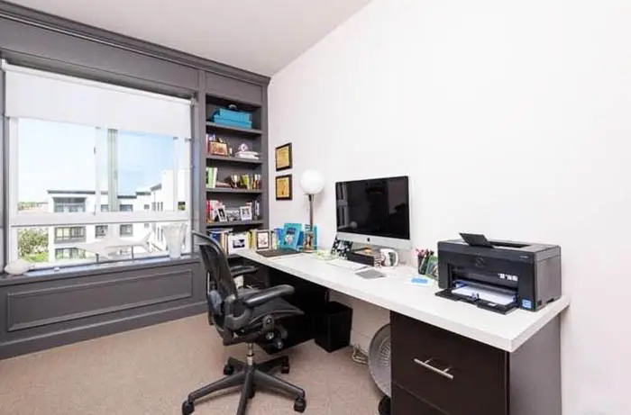 Window with white shade, gray shelves, printer and black executive chair