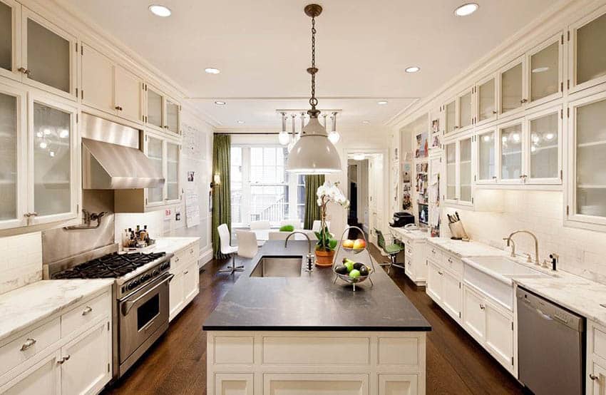 Kitchen with white cabinets and black soapstone countertop island with white tile backsplash and quartz main counters
