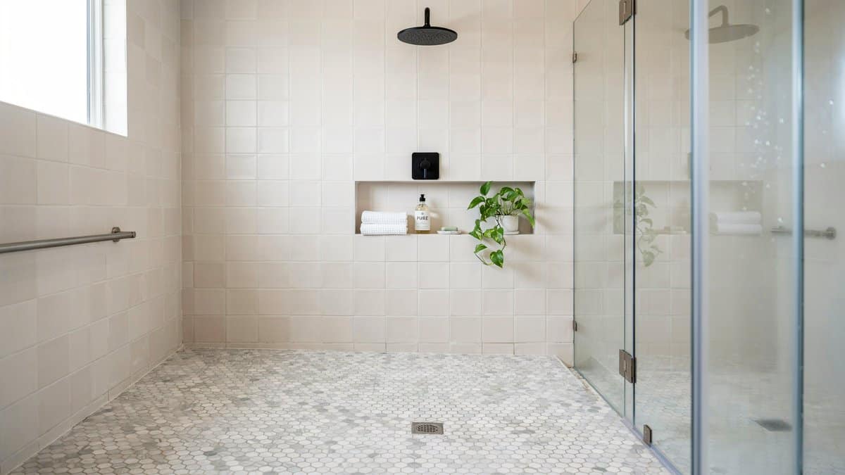 Walk-in shower finished with white penny sheet tile flooring and pale walls
