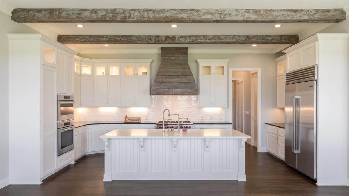 Two reclaimed barnwood beams spanning a white kitchen with weathered plank range hood and beadboard island