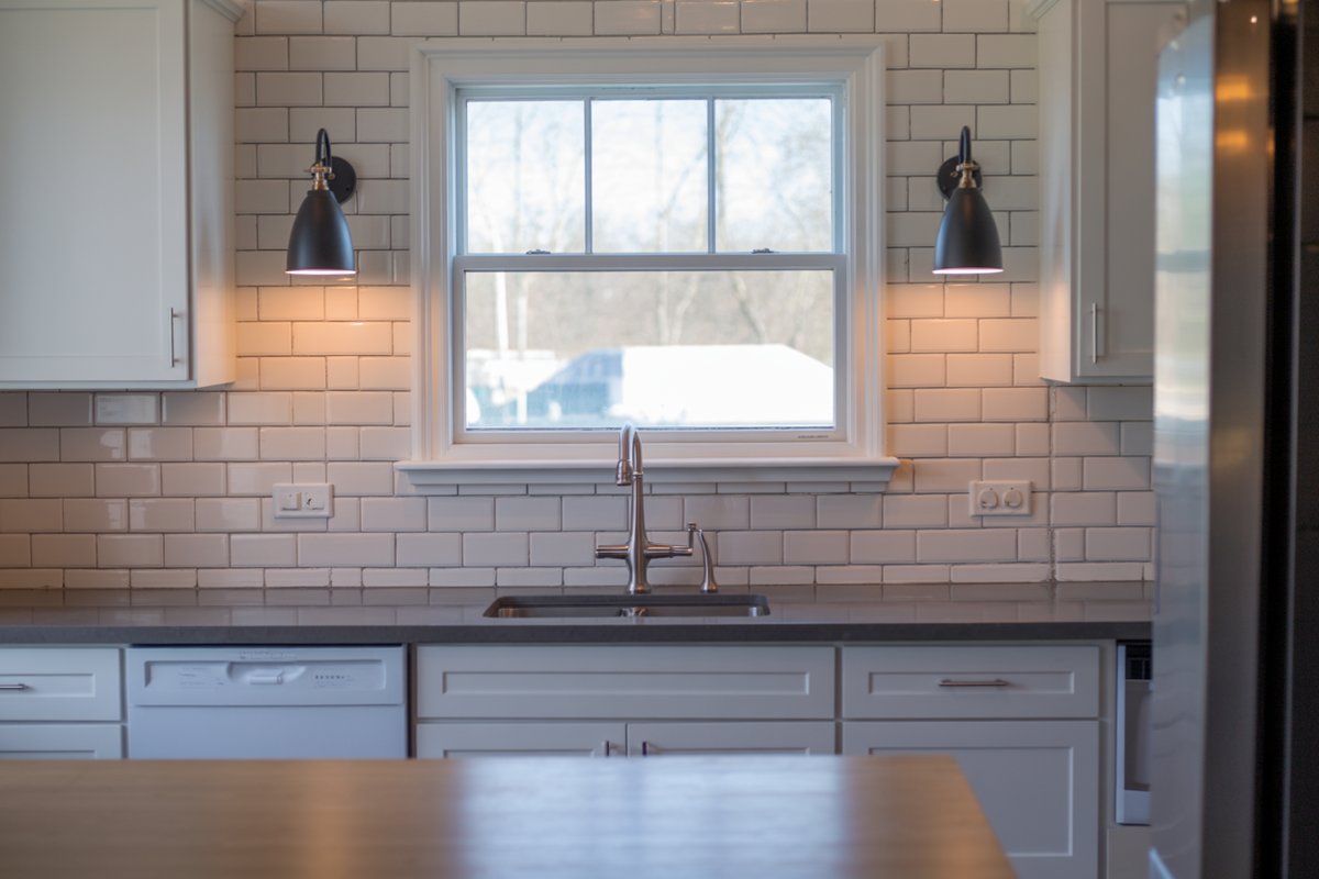 Two black wall sconces flanking a window above a subway tile sink wall