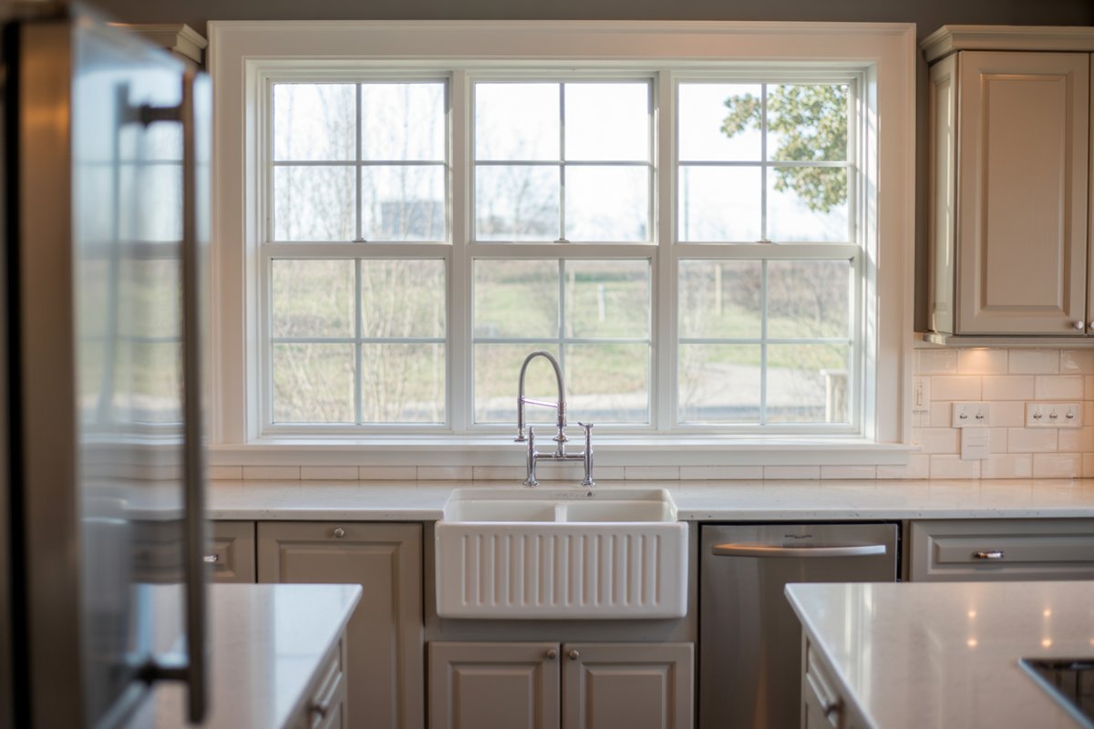 White farmhouse sink below a large grid picture window with countryside views