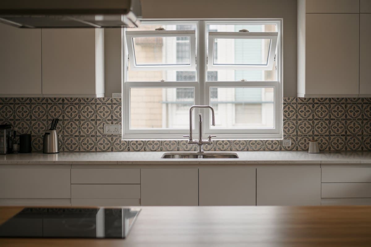 Open casement windows above a sink with a patterned blue tile backsplash
