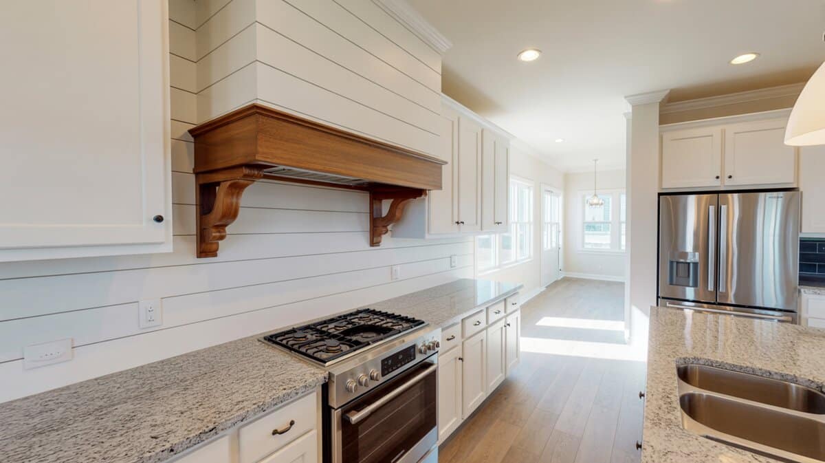 Custom white shiplap hood with wood shelf over the range beside granite counters