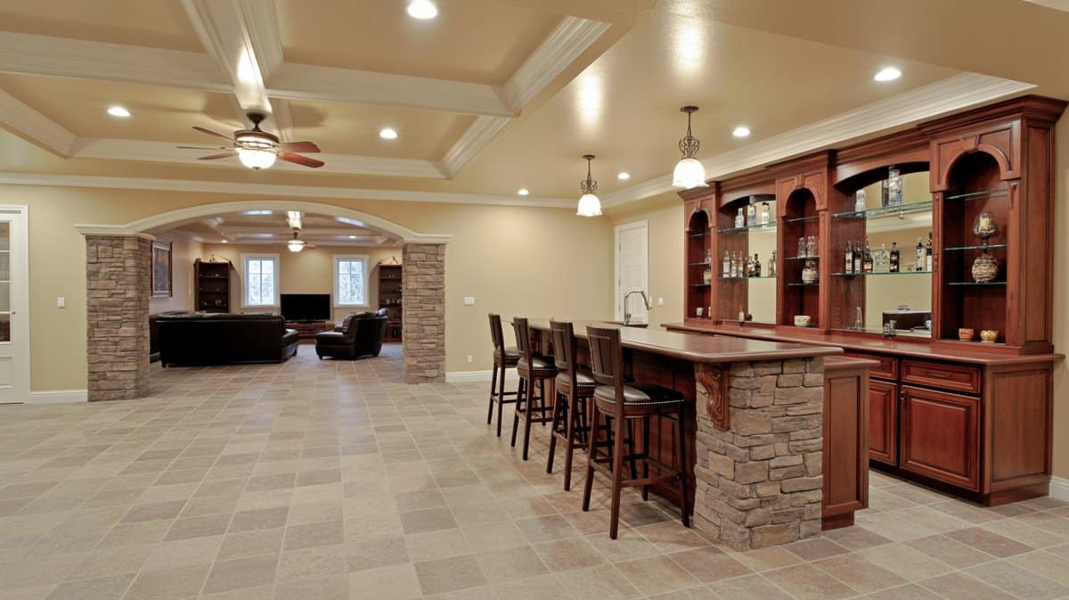 Luxury traditional basement with stone-wrapped bar peninsula, dark cherry cabinetry with arched shelves, and travertine tile floor