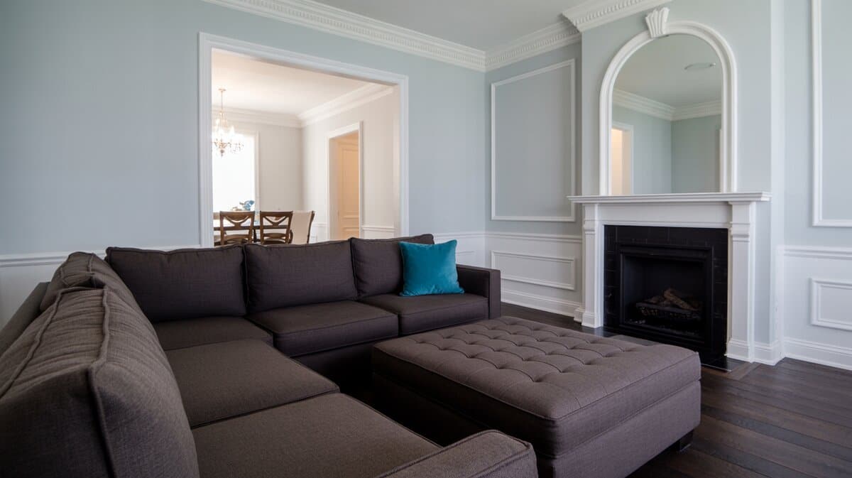 Charcoal sectional sofa with teal accent pillow against pale blue walls and white fireplace