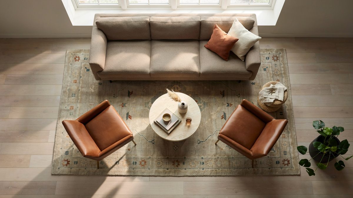 Overhead view of a beige patterned rug holding a sofa, two leather chairs and round table