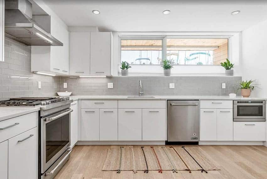 Kitchen with grey glass backsplash, flat door cabinets and under cabinet lighting