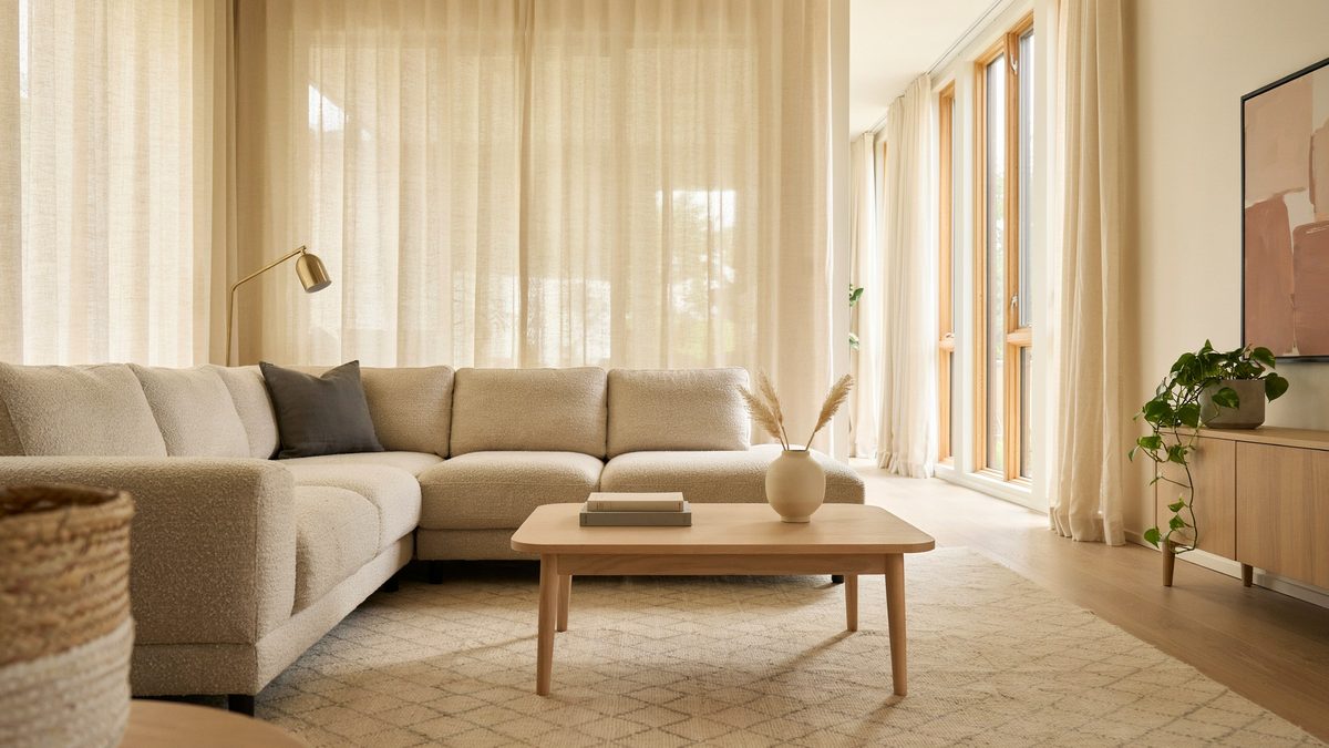Ivory sectional sofa and oak coffee table on a textured diamond weave rug beside sheer curtains