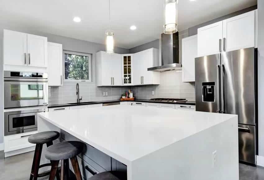White kitchen with small window above sink, gray tile backsplash and pendant lights above island