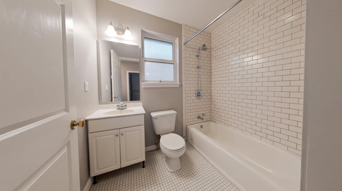 Compact full bathroom with white vanity, toilet, and subway tiled tub shower combo.