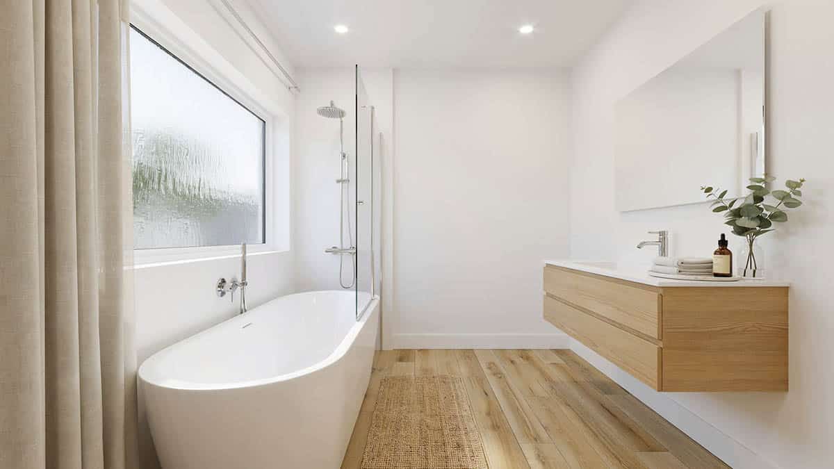 Freestanding tub with glass shower screen sits by a window over wood flooring.