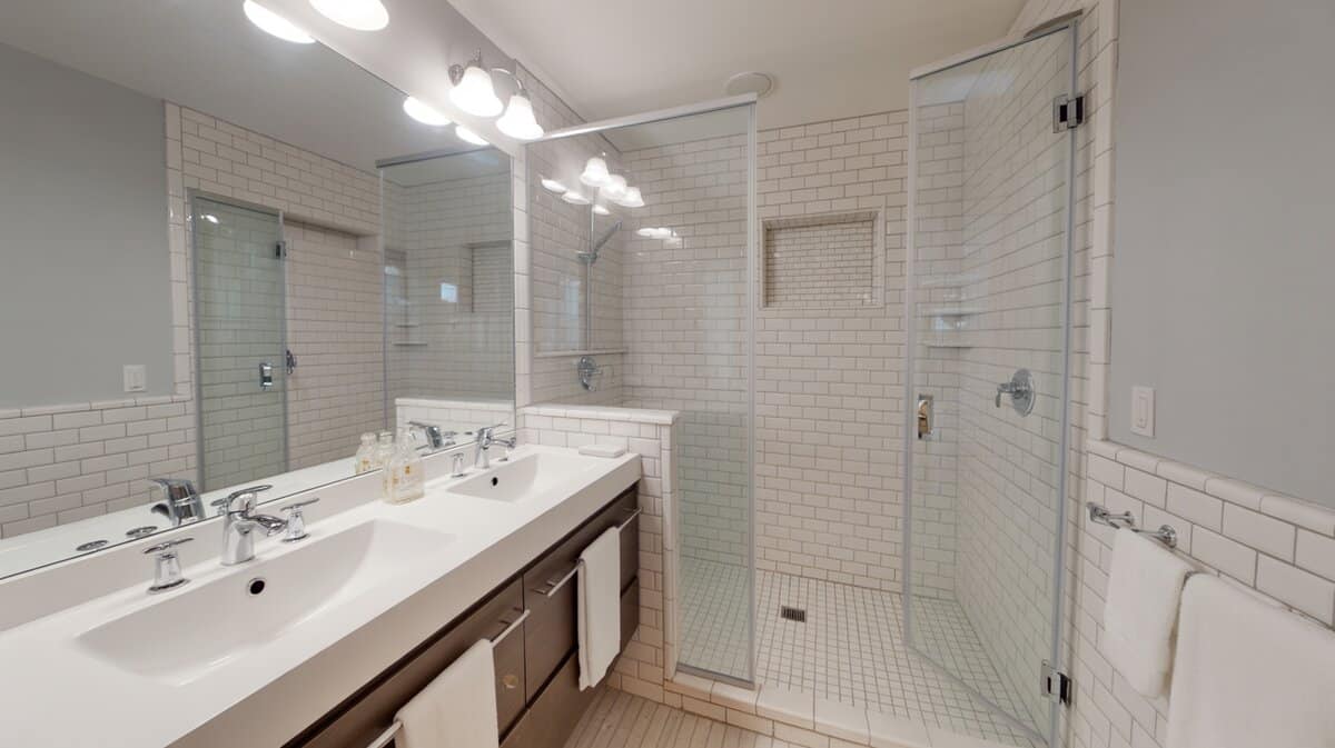 White double sink vanity faces a subway tiled walk-in shower with glass door.