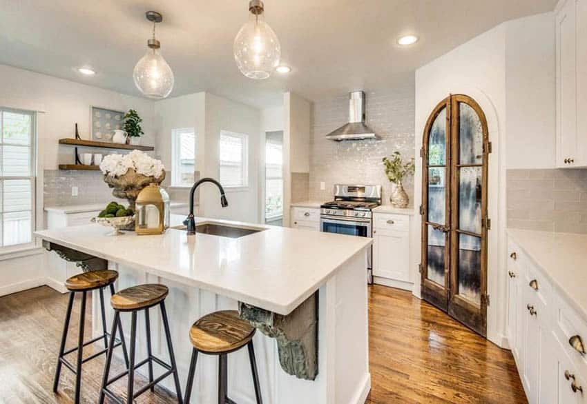 Kitchen with custom arched wood pantry door, white cabinets and white quartz countertops