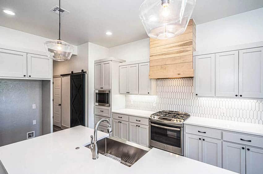 Kitchen with light gray cabinets, light wood oven hood and white quartz countertop