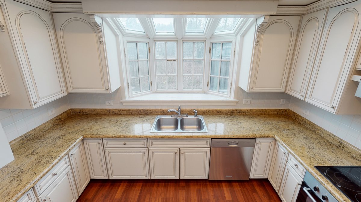 Antique white cabinets with gold granite countertops and a large bay window with skylight above the sink