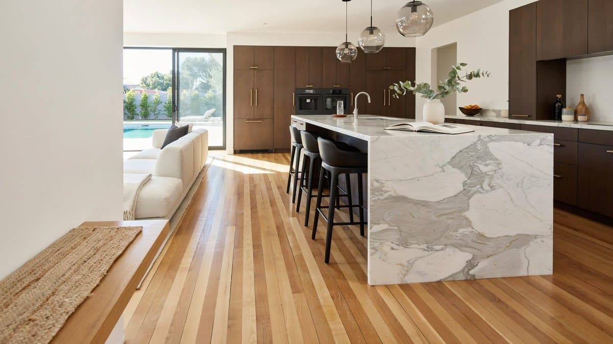 Open plan kitchen with dark brown cabinets, marble waterfall island and honey bamboo floors