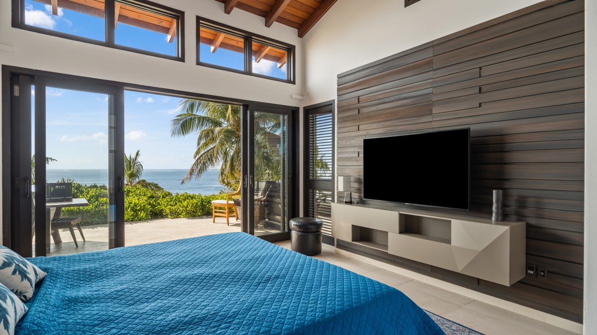 Tropical beach bedroom with blue quilted bedspread, vaulted wood beam ceiling, and folding glass doors to an ocean view