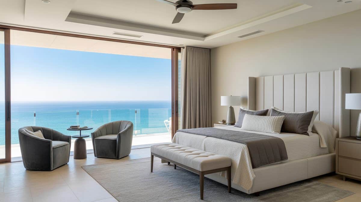 Coastal bedroom with tall channel-tufted headboard, ceiling fan, and ocean view through glass balcony doors