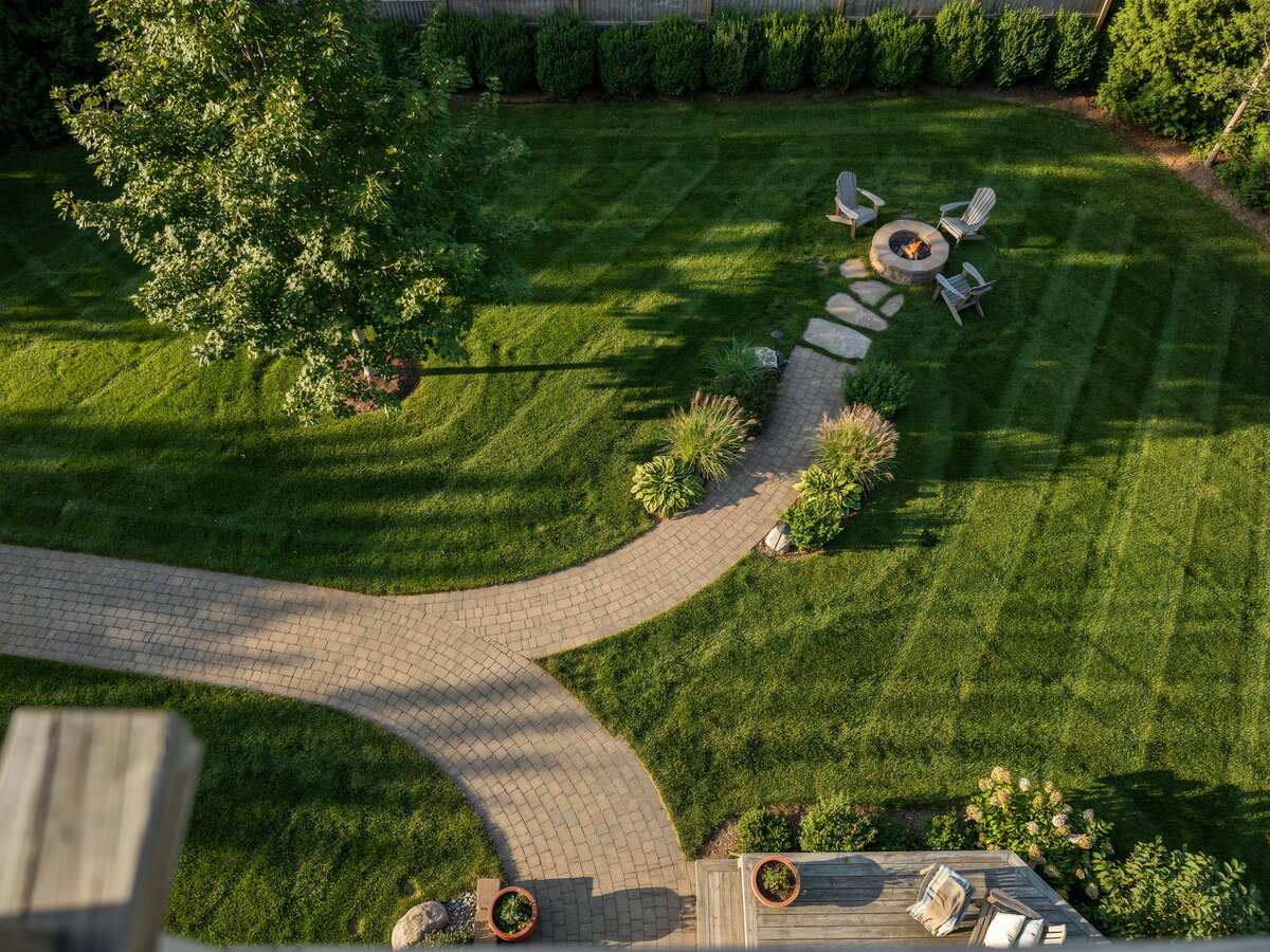 Aerial view of a curved cobblestone path winding to a fire pit seating area in a backyard