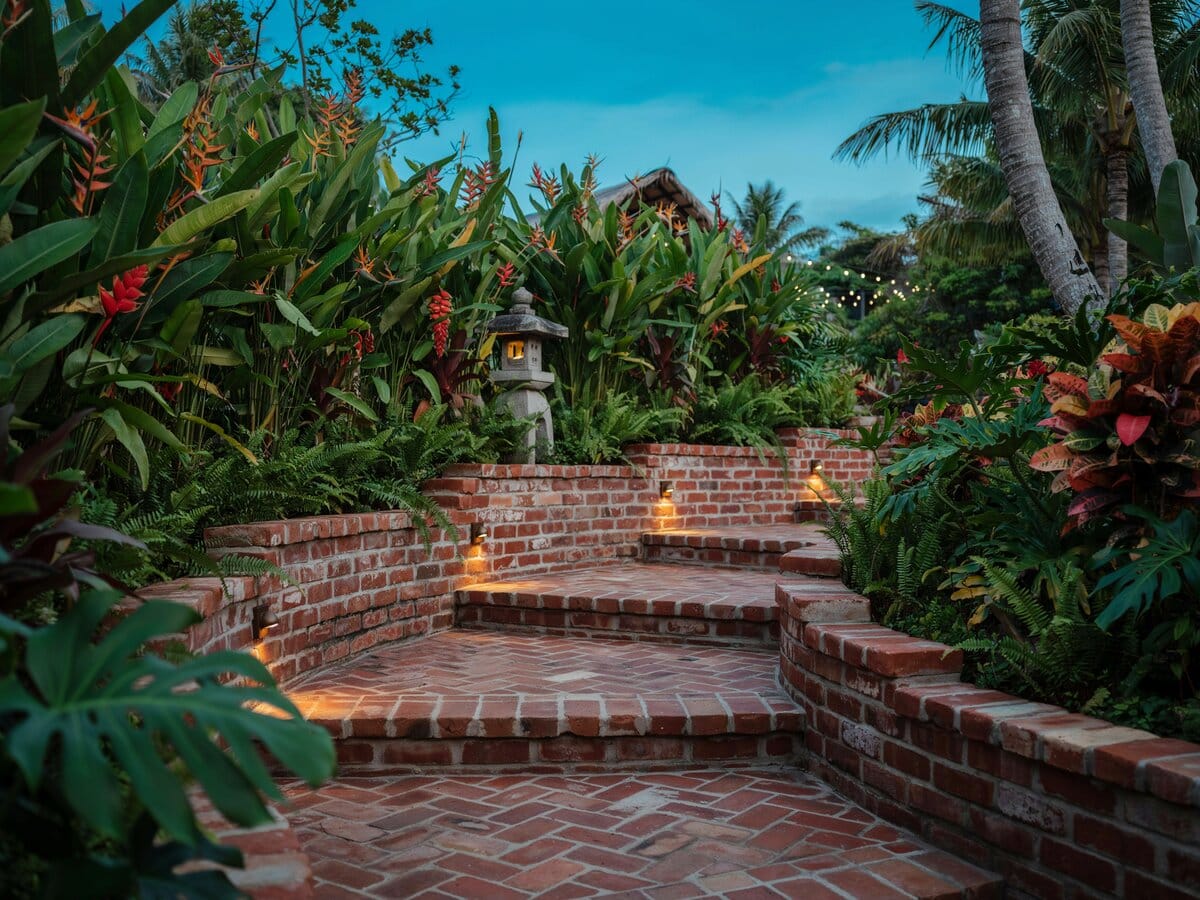 Tiered brick walkway steps with stone retaining walls and path lighting at tropical dusk