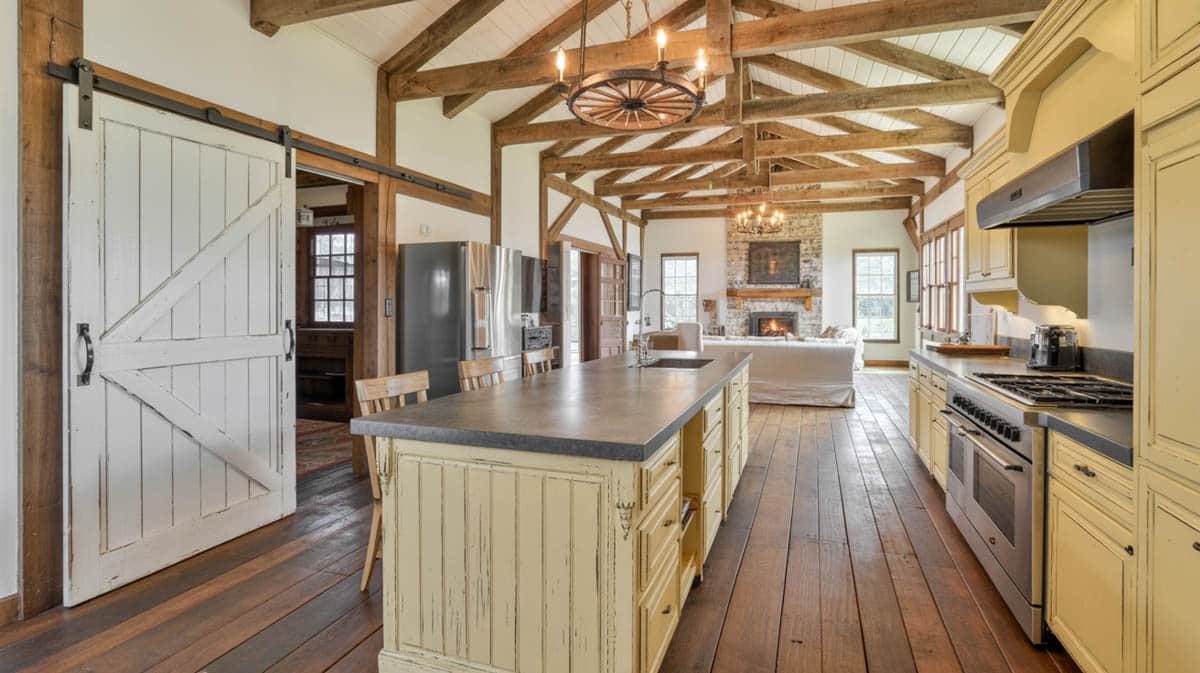 Open kitchen with cream cabinets, a sliding barn door, and exposed timber ceiling beams throughout