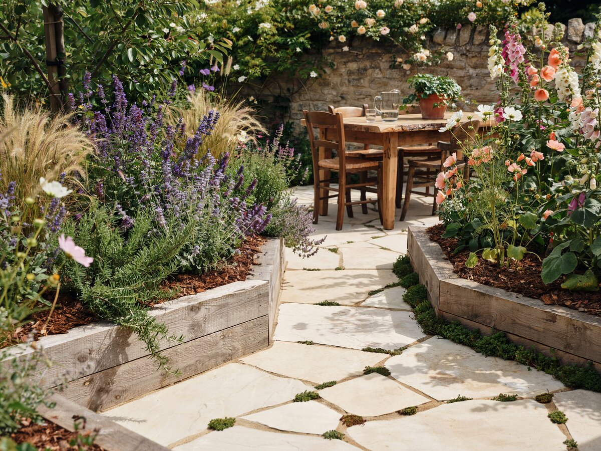 Cream flagstone path winding through a wild cottage garden with mulch beds and outdoor dining