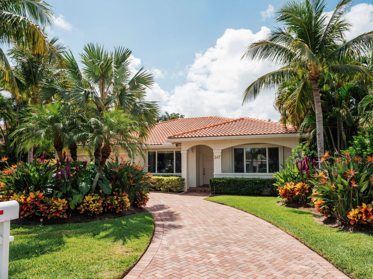 Curved brick paver path beside a Florida ranch home with tropical landscaping and palm trees