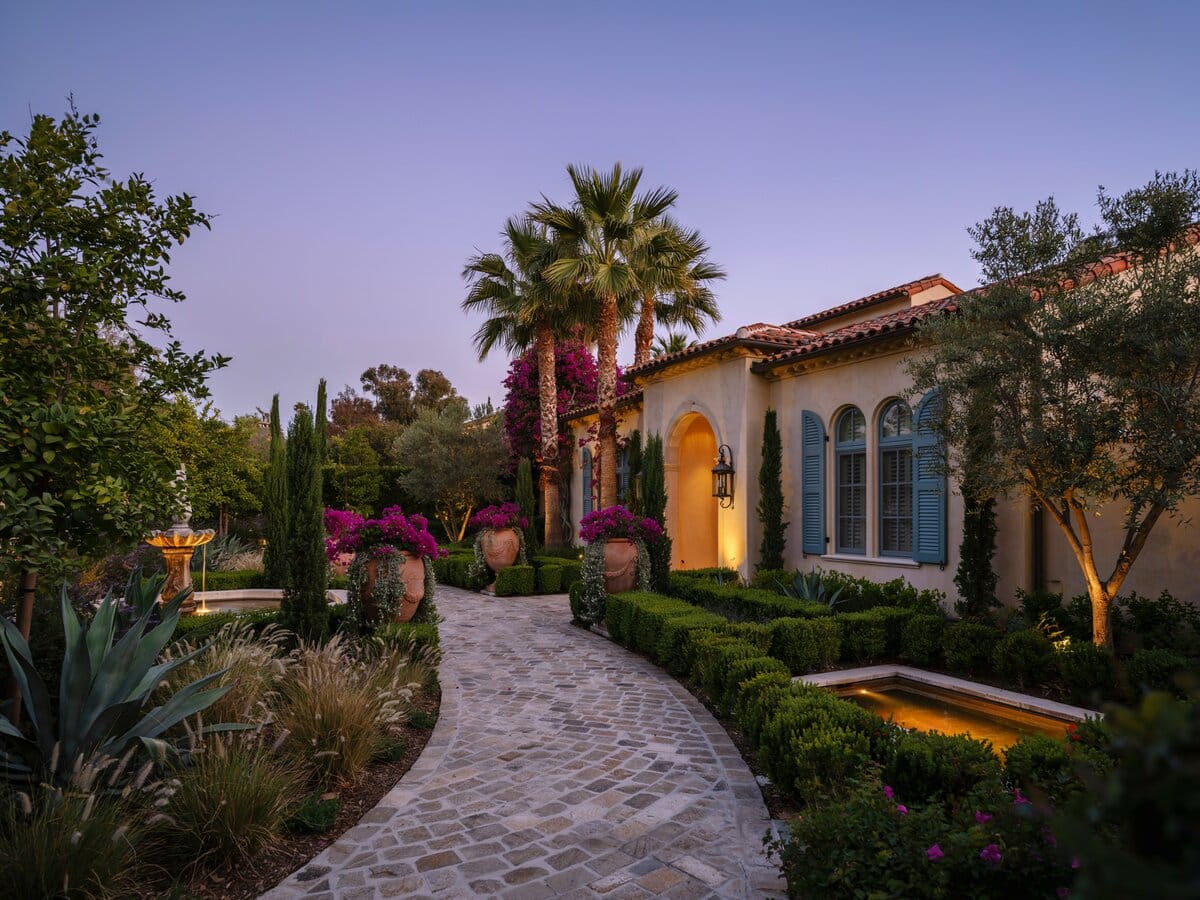Curved cobblestone path winding around a Mediterranean style home with palm trees at dusk
