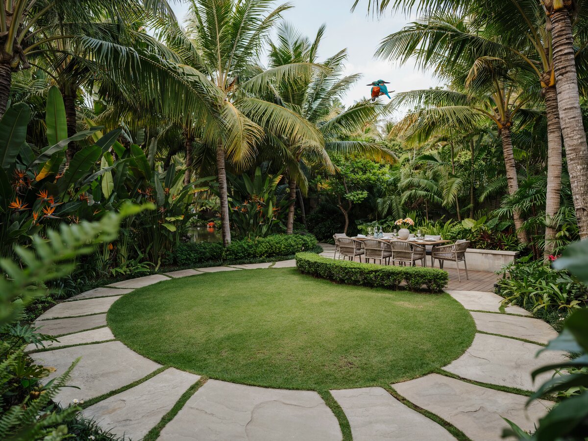Curved flagstone walkway skirting a round manicured lawn leading to an outdoor patio dining area