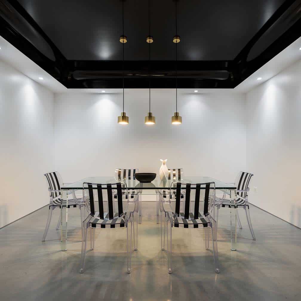Modern dining room with a glossy black paneled ceiling above a glass table with acrylic chairs.