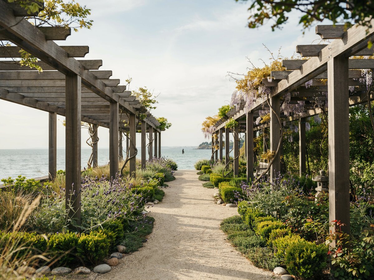 Gravel and stone walkway beneath a series of wood pergolas at a waterfront property
