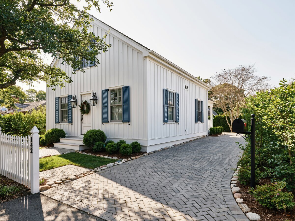 Gray herringbone brick paver walkway beside a white coastal cottage with navy shutters and picket fence