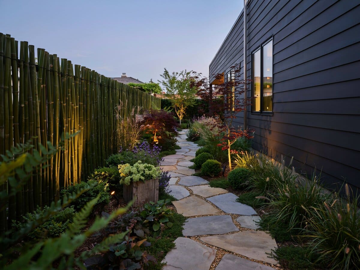 Irregular flagstone path through a side yard beside a modern dark gray home with uplighting at dusk