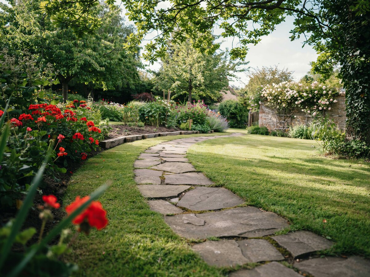 Irregular flagstone stepping stones along a curved garden border with bright red flowers