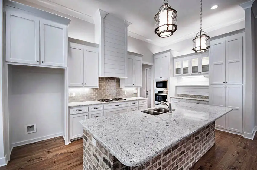 Kitchen with white cabinets rustic brick island and wood flooring