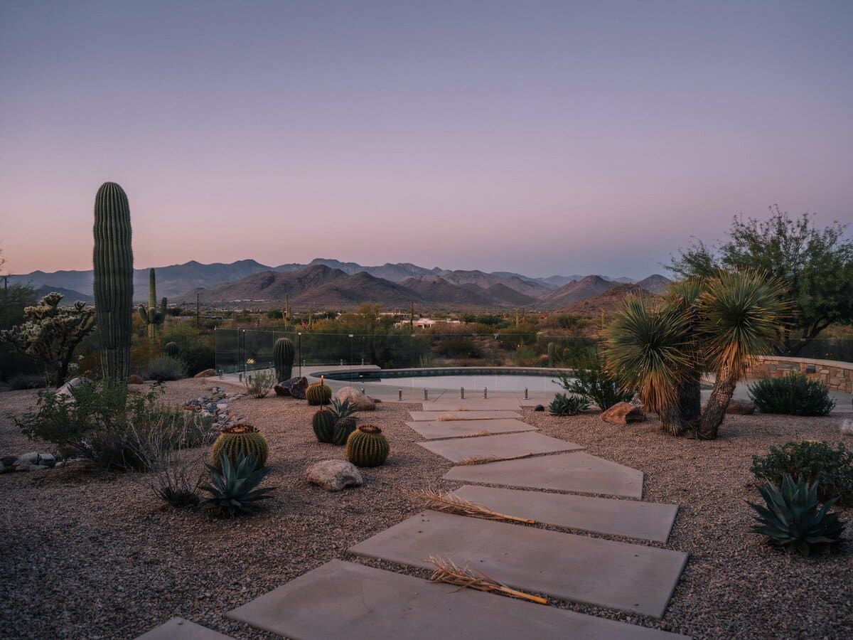 Large concrete stepping slabs through a gravel desert backyard with cactus and a mountain view at dusk