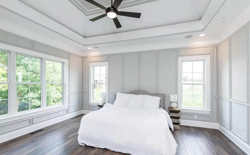 Master bedroom with modern black ceiling fan, gray wall paneling and tray ceiling
