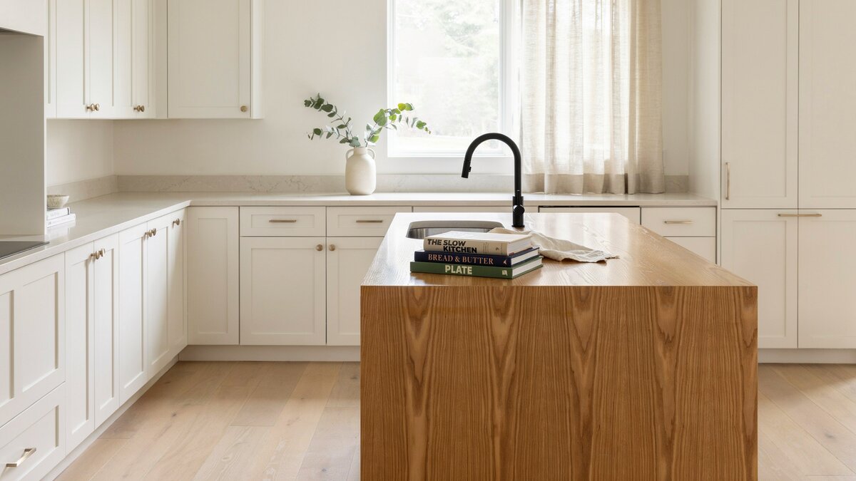 Stack of cookbooks displayed on wood veneer island in modern white kitchen