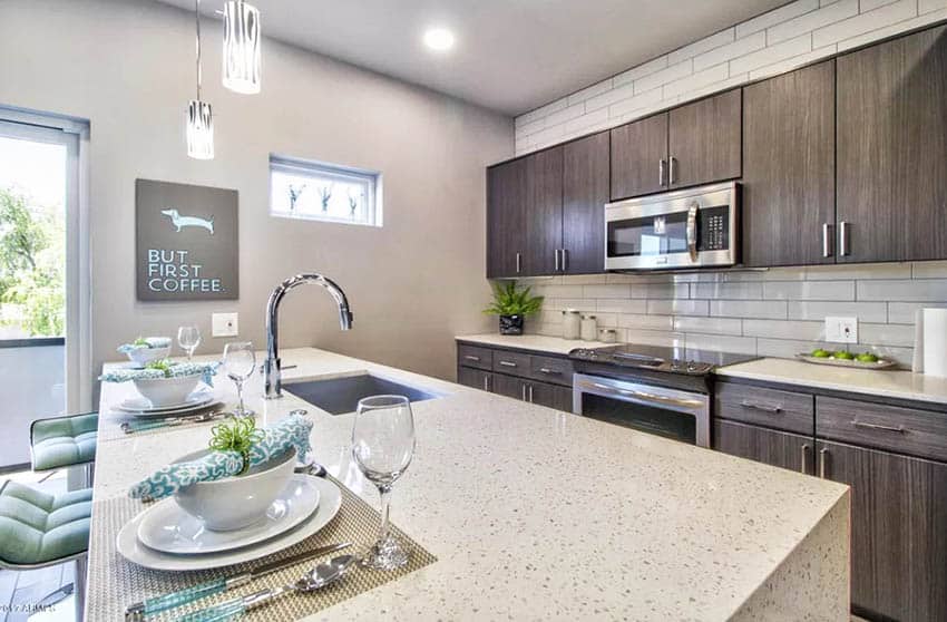 Open galley style kitchen with dark cabinets white quartz counter and decor bottles