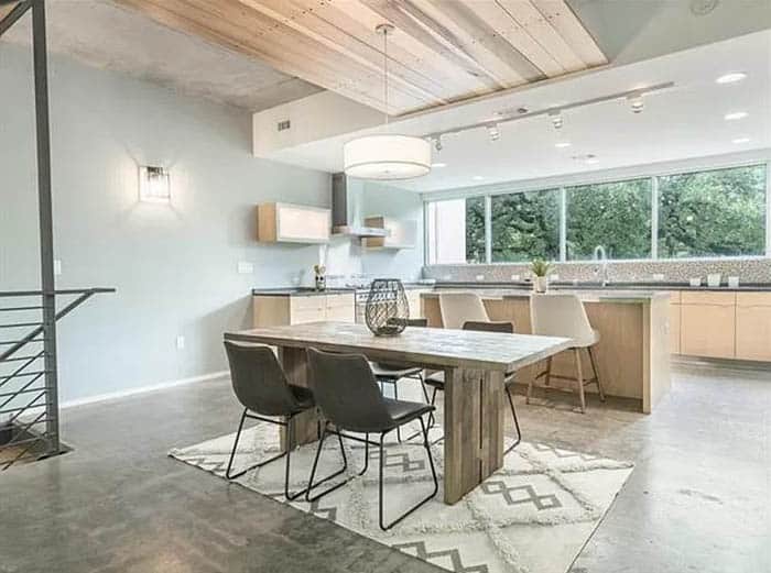 Open kitchen dining room with pale green walls gray concrete floors light brown cabinets