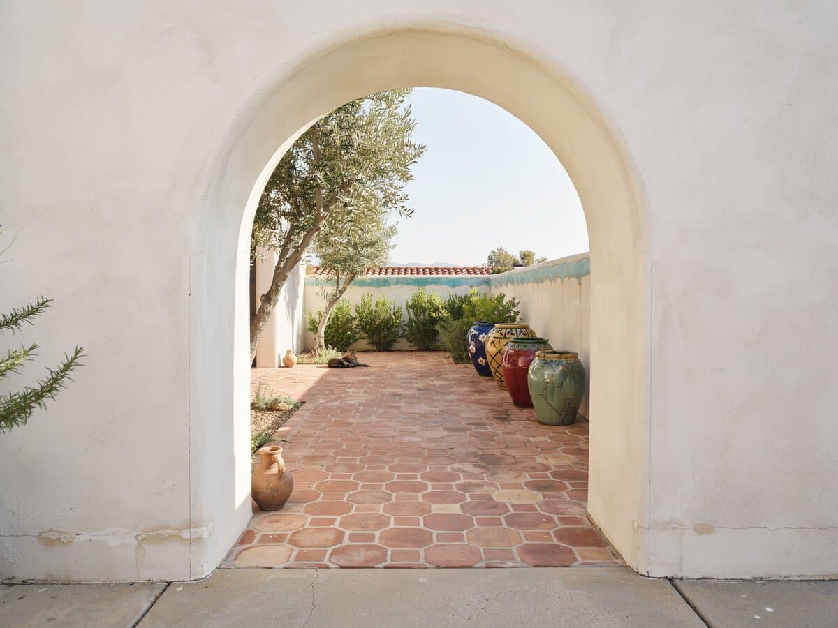 Red hexagonal terracotta tile walkway passing through a white stucco arch into a Southwest courtyard