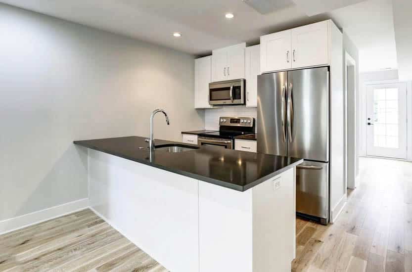 kitchen with white recessed cabinets, black countertops, and subway tile backsplash